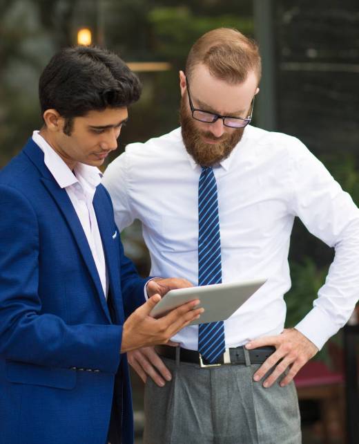 Pensive concentrated managers standing in modern cafe and analyzing online data. Indian assistant in formalwear showing report to bearded executive. Technology concept